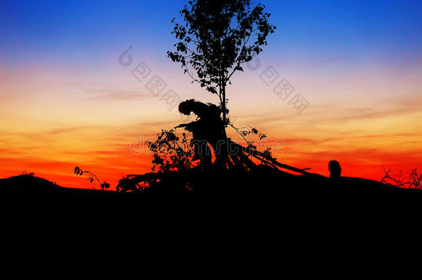 夕阳的美丽景色与坐在树枝上的人和孩子的黑暗剪影。