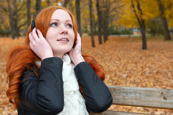 女孩用耳机在音频<strong>播放器</strong>上听<strong>音乐</strong>，坐在城市公园的长凳上，秋天的季节，黄树和落叶