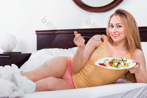 穿着内衣的金发女人坐在床上享受沙拉