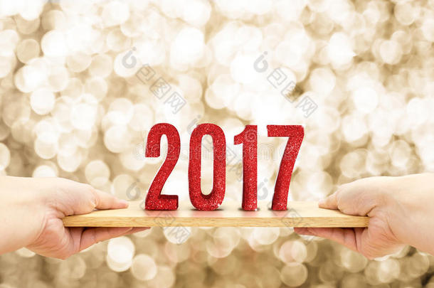 手拿木板与2017年快乐的新年红色闪光号码在模糊的金色闪闪发光的波克灯