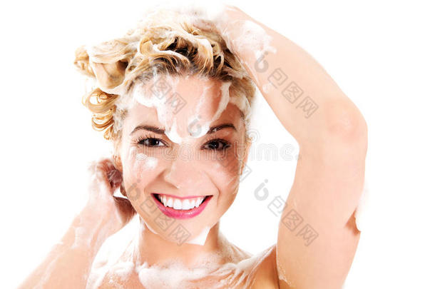 美丽微笑的年轻女人用洗发水洗头发-隔离在白色上。