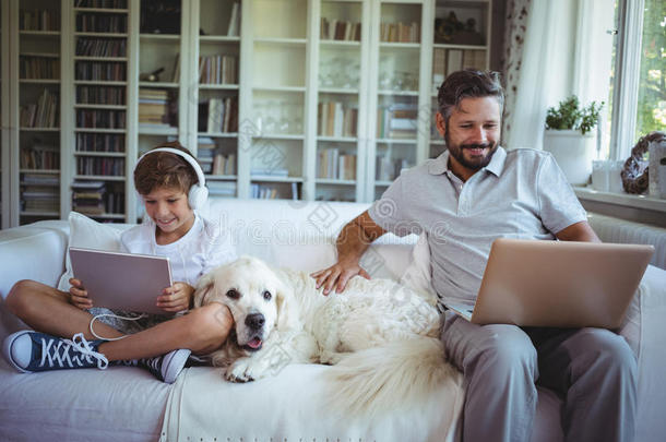 父子俩坐在沙发上，用数码平板电脑和笔记本电脑