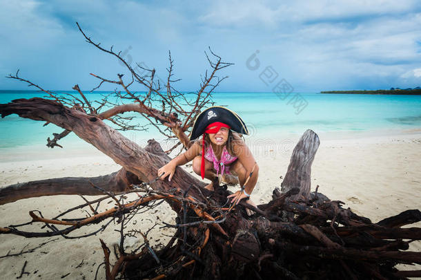 惊人的有趣，愤怒的小女孩海盗坐在海滩上的老枯树上，在黑暗的戏剧天空和海洋背景下