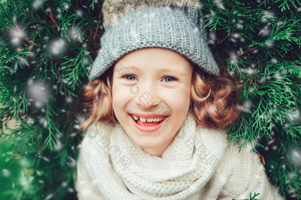 关闭冬季肖像快乐的儿童女孩戴着温暖的针织帽和围巾与圣诞树