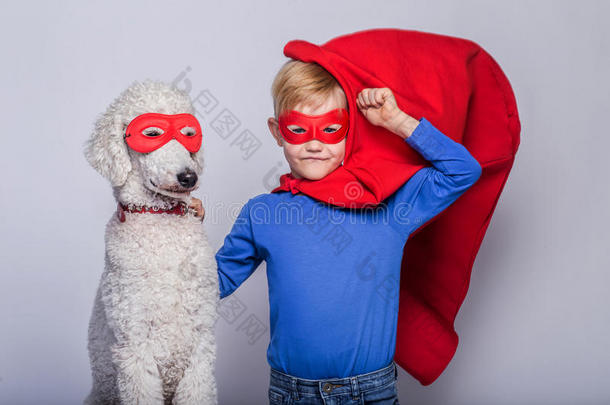 英俊的小超人带着狗。 超级英雄。 万圣节。 白色背景下的工作室肖像