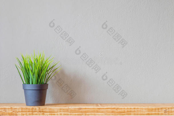 绿色的草在一个黑色的塑料壶上，靠在墙上的木架子上