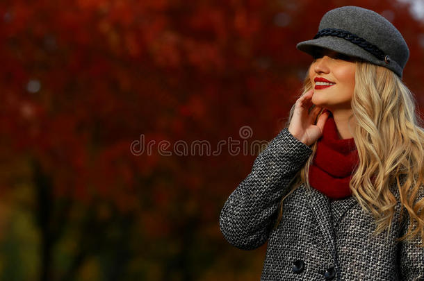 美丽的女人在秋天的公园微笑。 红色枫树花园背景。 向框架的左边看向空白复制空间