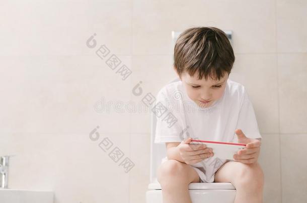 坐在马桶上玩智能手机的男孩。