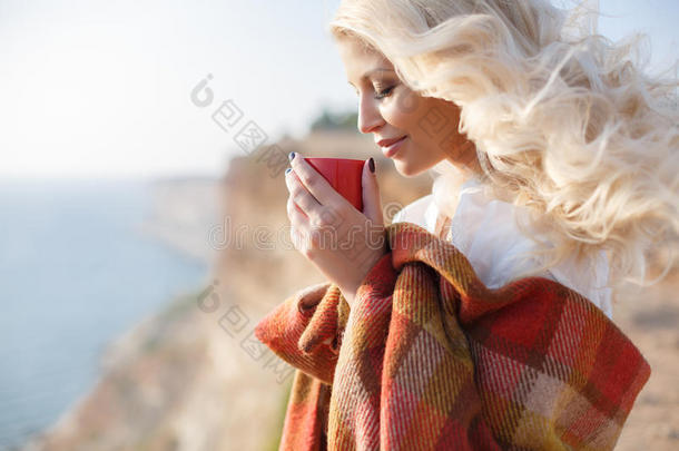 坐在岩石海岸上喝咖啡的漂亮女人