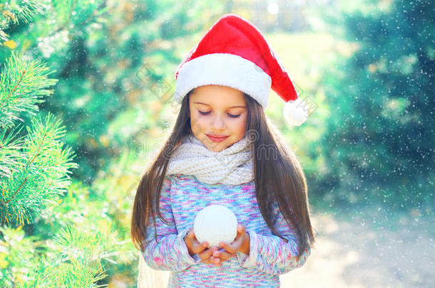 圣诞小孩戴着圣诞红帽子的小女孩在树枝旁抱着雪球