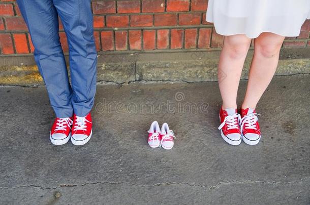 在婴儿运动鞋旁边穿红色运动鞋的成年人的形象。 怀孕和期望概念。