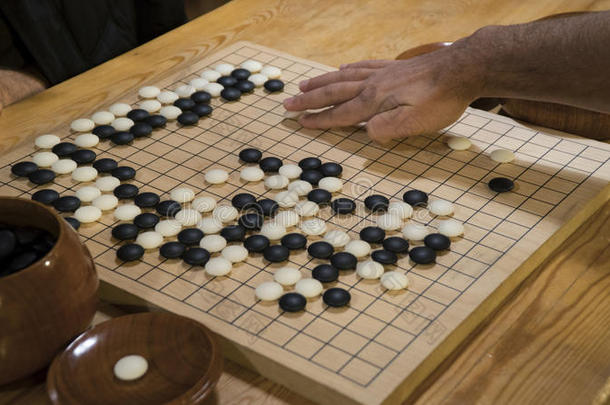 手在中国围棋或围棋游戏板上玩黑白。 室内活动与人工光。