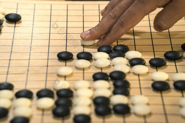 手在中国围棋或围棋游戏板上玩黑白。 室内活动与人工光。