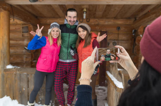 女孩在智能手机上拍照，人们组木乡村山屋冬季雪度假村