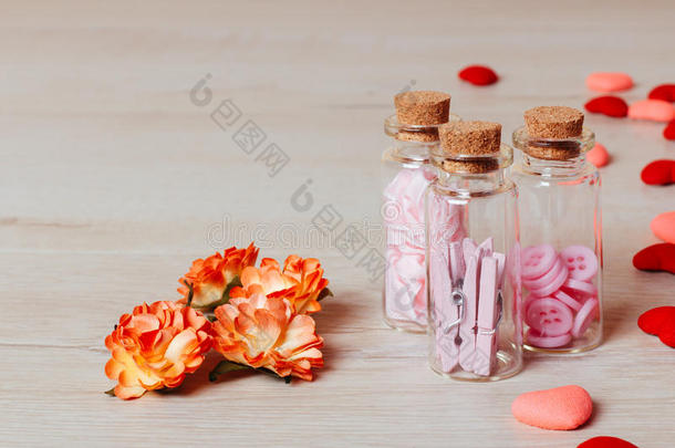 关闭明亮的小心脏，春天的花朵和玻璃瓶，包含衣架和按钮在木制背景。