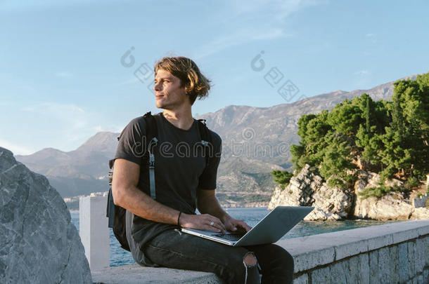 迷人的年轻人在海边的笔记本电脑上工作，自由职业，社交网络和网上购物的概念