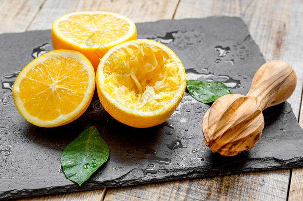 把橘子切成两半，在木制背景上用榨汁机榨汁