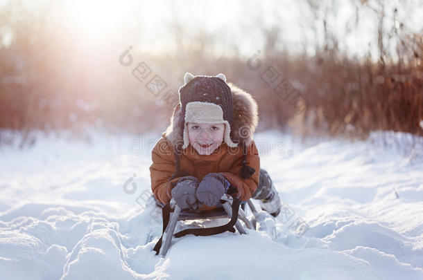 可爱的小有趣的孩子男孩穿着温暖的冬天的衣服，在雪撬上玩，在下雪天的户外玩。