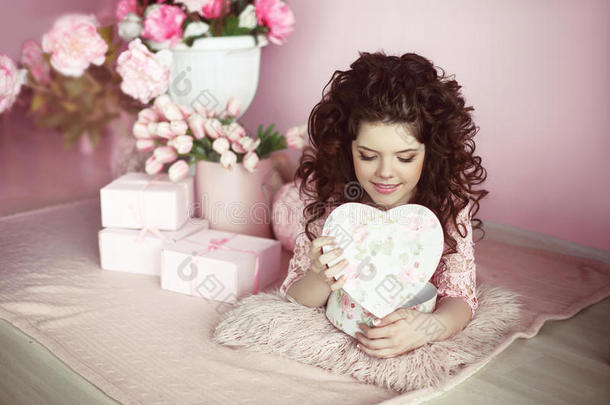 美丽的年轻肖像开放礼物，浪漫惊喜。 黑发的粉红色连衣裙在花束和礼品盒上