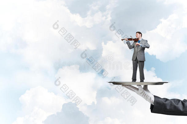 商人在金属托盘上在蓝天背景下拉小提琴