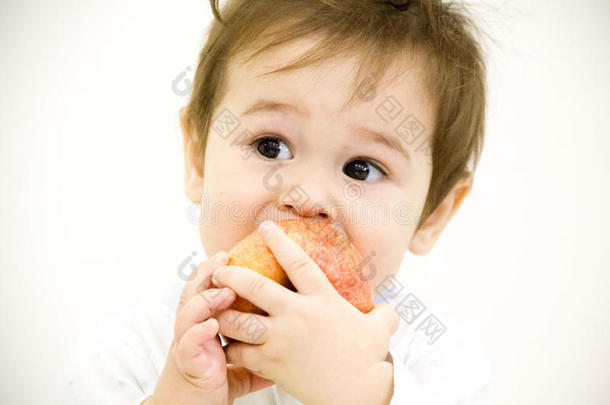 小男孩坐在桌子上，拿着水果和蔬菜，吃着白底隔离的苹果