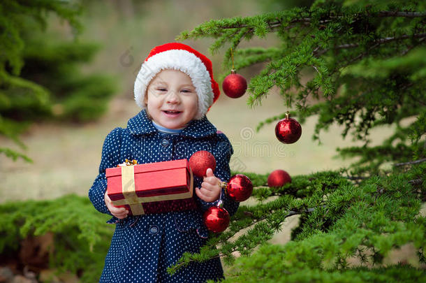 美丽的小女孩戴着圣诞老人的帽子，拿着礼物盒，在圣诞树附近微笑