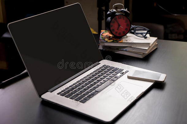 办公室桌子上的空白笔记本电脑屏幕上有时钟和电话。