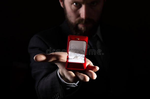 穿着西装的胡子男人在红色的<strong>盒</strong>子里给了一个<strong>戒指</strong>，并在黑暗的背景下表达了不同的情感