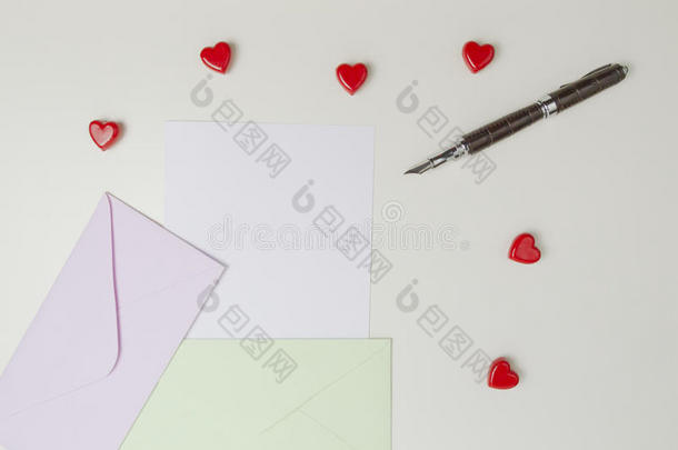 白色桌子上的信封、留言、钢笔和小红心。 情书情人节概念