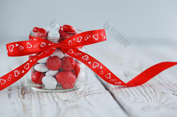 五颜六色的糖果罐装饰着红色的蝴蝶结，白色的木制背景上有心形。