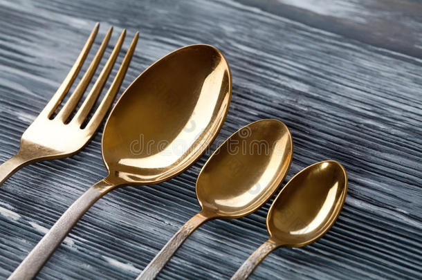金色的勺子和叉子在灰色的木制背景上。 带有划痕擦伤的老式餐具。 柔和的焦点。 宏观观点。