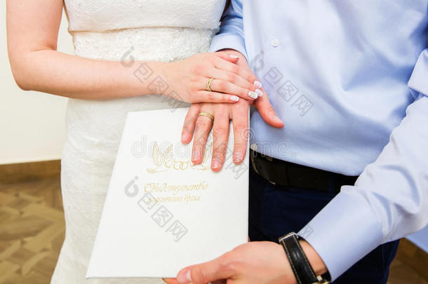 `结婚证上有结婚戒指的手`。 外国俄罗斯文本-结婚证