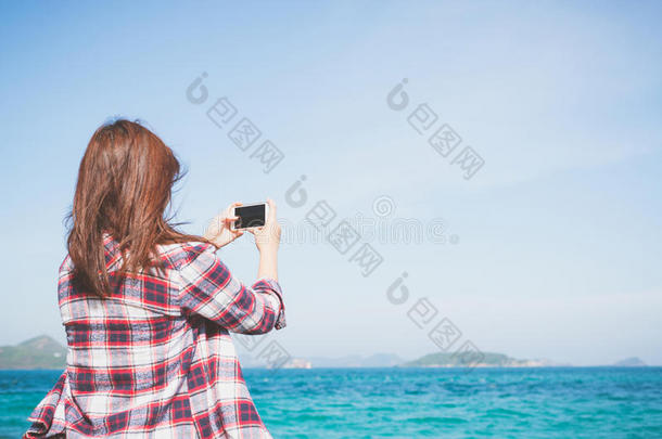 在海滩的地平线上，一个女人用智能手机相机拍照的后视图。