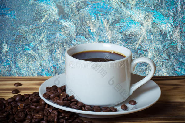 咖啡豆和咖啡在白色的杯子在木桌上，相反，美丽的自然图案在磨砂玻璃上作为背景。