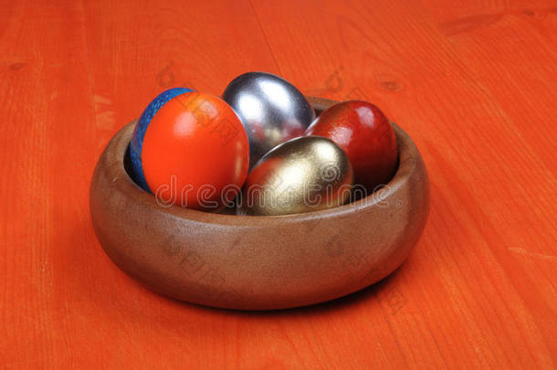 复活节作文。 五颜六色的鸡蛋在一个木制碗在一个橙色的木制背景。
