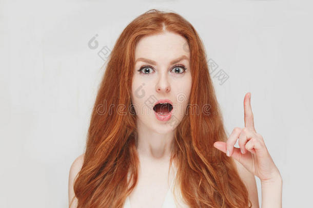 美丽的红头发惊讶的女人拿起手指。 在白色背景上。 表情积极的面部表情。
