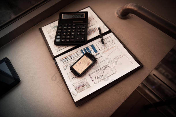 文件夹与财务分析图表。 电话`屏幕上的图表，接下来是计算器和钢笔