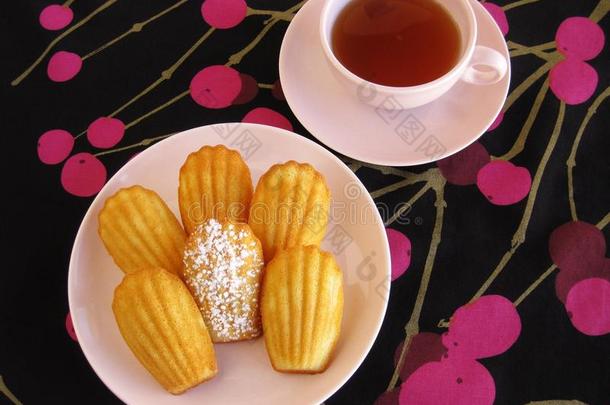 法国马德兰和茶在粉红色老式餐具上的黑色和洋红色樱桃图案桌布