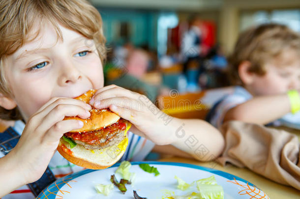 可爱健康的学龄前男孩坐在<strong>学校食堂</strong>吃汉堡包