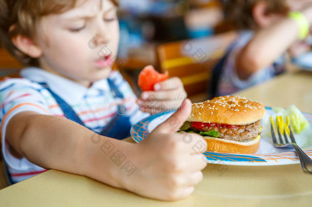 可爱健康的学龄前男孩坐在<strong>学校食堂</strong>吃汉堡包