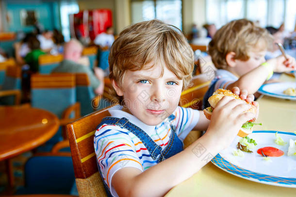 可爱健康的学龄前男孩坐在<strong>学校食堂</strong>吃汉堡包