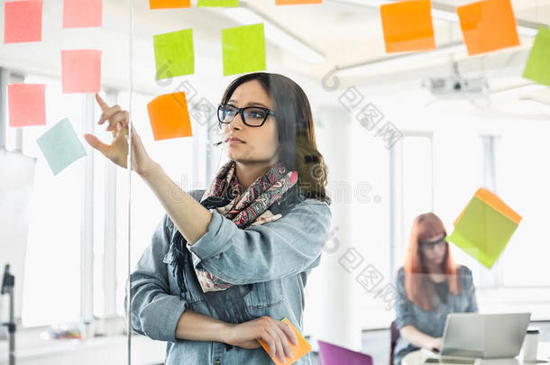 有<strong>创意</strong>的女商人和同事在办公室后台阅读玻璃<strong>墙</strong>上的便条