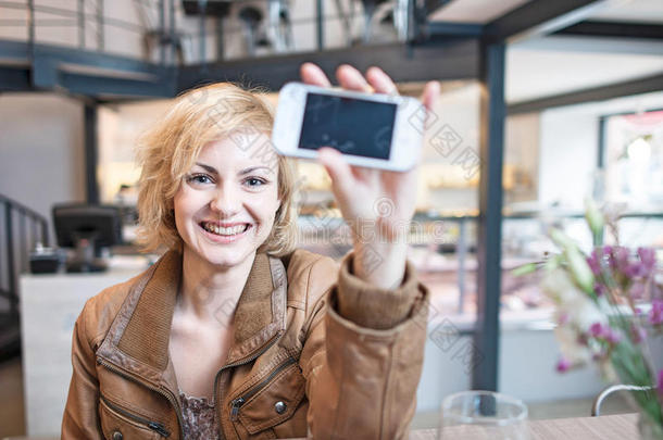 微笑的年轻女子在咖啡厅展示手机