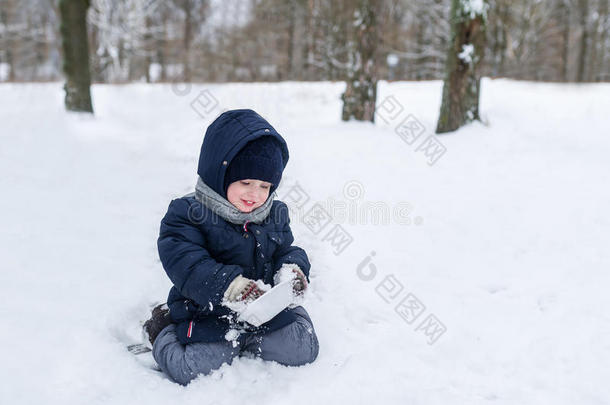 冬天可爱的小男孩坐在公园的雪地里男孩擦盘