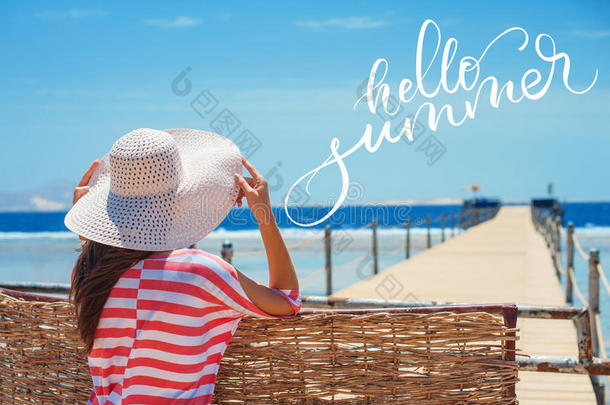 特写背面的女人戴着白色的帽子，朝蓝色的海洋和天空看，并说你好夏天。 书法