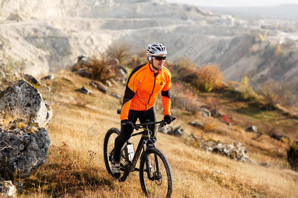骑自行车的骑着橙色夹克的骑自行车的洛基山。 极限运动概念。 文本的空间。
