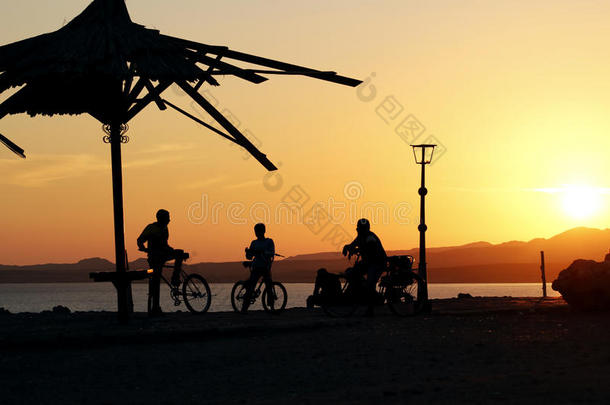 日落时在海滩上骑自行车的剪影孩子