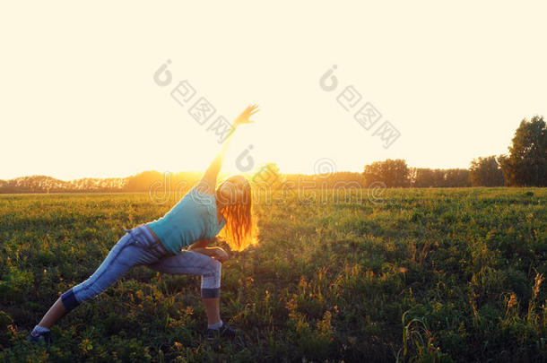 美丽的年轻女人在田野上做瑜伽运动，在惊人的日落。 瑜伽的概念。