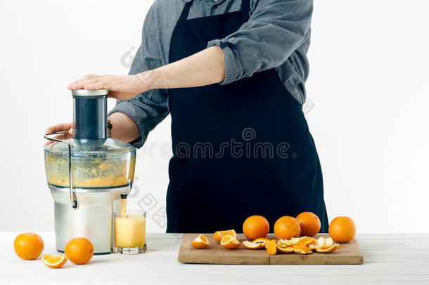 匿名男子穿着围裙，准备健康的橙汁，使用<strong>现</strong>代电动<strong>榨</strong>汁机，健康的生活方式概念
