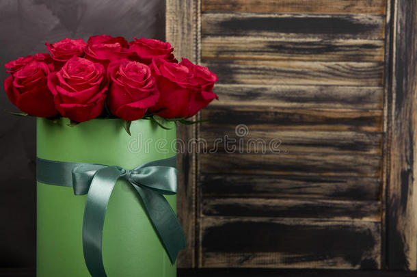一束精致的红色玫瑰，绿色礼品盒，深灰色的乡村木制背景。 <strong>家居装饰</strong>。